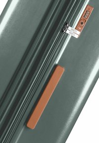 Valigia rigida di colore verde scuro con finitura lucida. Presenta una doppia cerniera e una maniglia con accento marrone. È visibile una serratura a combinazione.