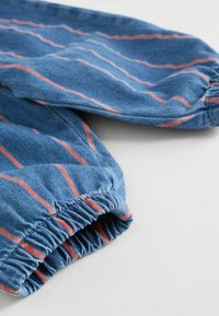 Plava traper tkanina s elastičnim manšetama, s tankim narančastim prugama koje se horizontalno protežu. Tekstura izgleda mekano i ležerno.