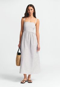 Dryžuota maksi suknelė su kvadratiniu iškirpimu ir plonomis petnešėlėmis, pagaminta iš lengvos medžiagos. Suderinta su pintu krepšiu ir plokščiomis šlepetėmis.