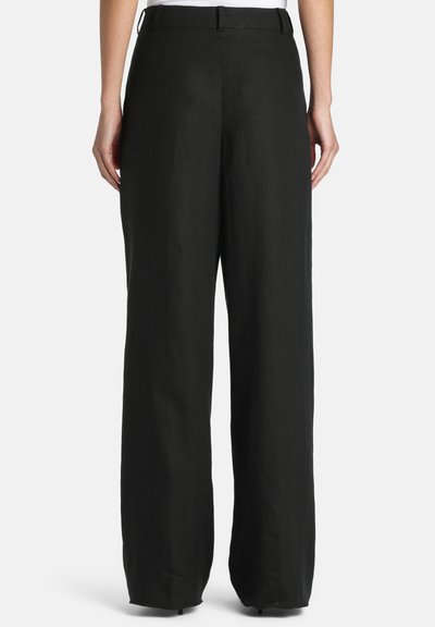 Hátsó nézet egy személyről, aki magas derekú, széles szárú fekete nadrágot visel övbújtatókkal és egy fehér inget betűrve.