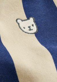Blue and beige striped fabric with a small embroidered white bear face outlined in gray centered on the beige stripe.