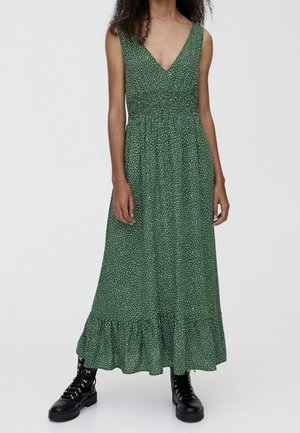 Femme portant une robe maxi verte sans manches à pois blancs avec un ourlet à volants, associée à des bottes de combat noires à lacets.