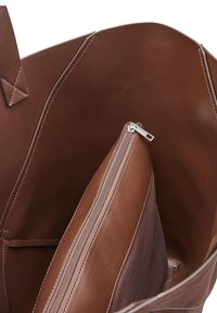 Braune Leder-Shopper-Tasche mit glatter Textur. Verfügt über ein Innenfach mit Reißverschluss und ein zusätzliches Fach. Minimale Nahtdetails.