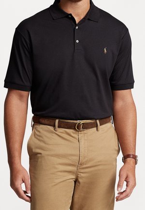 Homme portant un polo noir à manches courtes, un pantalon beige, une ceinture marron et une montre-bracelet marron.