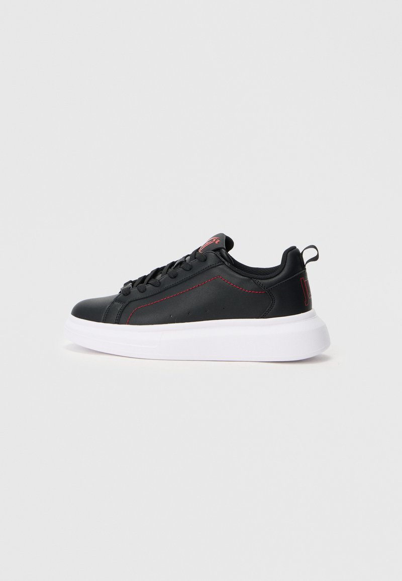 Schwarzer Tiefschnitt-Sneaker mit rotem Nähten, schwarzen Schnürsenkeln und dickeweißer Sohle, von der Seite auf einem schlichten grauen Hintergrund betrachtet.