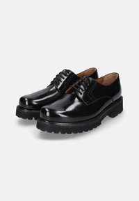 Een paar gepolijste zwarte leren veterschoenen met dikke robuuste zolen op een effen lichte achtergrond.