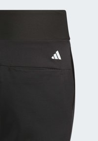 Černé sportovní kalhoty s vysokým pasem, hladkým povrchem, malým bílým logem poblíž pasu a detailem boční kapsy.