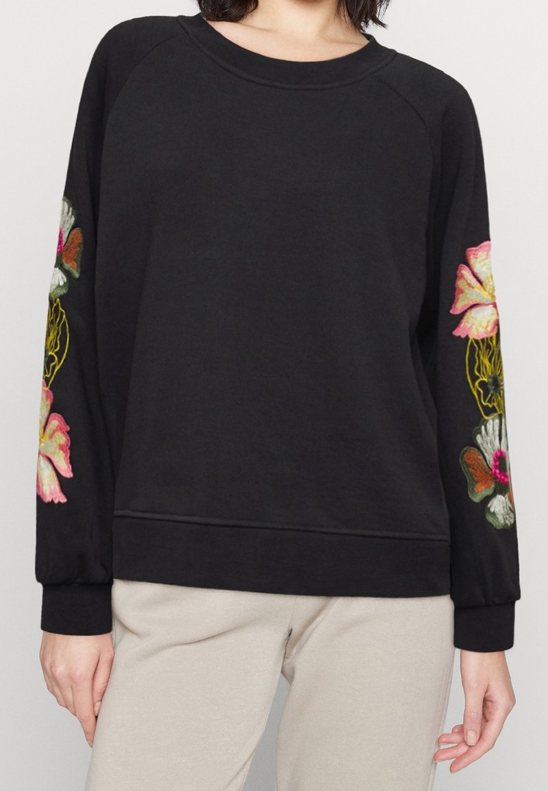 Sudadera negra con bordado floral en rosa y blanco en las mangas, cuello redondo y dobladillo acanalado. Tejido suave con un corte holgado.