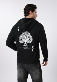 Μαύρο hoodie με μεγάλο λευκό γραφικό σπαθί στην πλάτη, διακοσμημένο με περίπλοκα σχέδια και το κείμενο "Τύχη και Δύναμη".