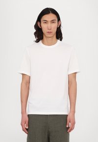 White cotton t-shirt with short sleeves, round neckline, and small logo detail on the chest. Simple and plain design with no patterns.