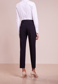 Marineblauwe tailored trousers met een rechte snit, voorzien van een gladde stoftextuur en een hoge tailleband. Gecombineerd met een witte blouse met kraag en nude hakken.