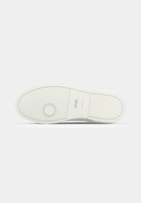 Semelle de chaussure blanche avec motif de bande de roulement circulaire près des orteils, logo "BOSS" et texte "Fabriqué en Italie" sur une surface plane.