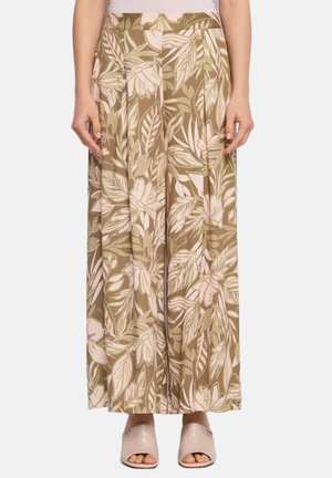 Pantaloni beige a gamba larga con grande stampa floreale bianca e verde chiaro, indossati con scarpe slip-on trapuntate rosa chiaro con punta aperta.