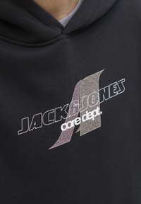 Haut à capuche noir avec un graphisme sur le devant affichant "JACK&JONES" en lettres blanches épaisses et "core dept." en texte plus petit. Le texte présente des accents gris et rose.