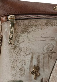 Braune Ledertasche mit einem strukturierten, metallisch-beigen Panel mit Säulendesign und einer bronzefarbenen Katzenanhänger-Detail. Reißverschlussverschluss.