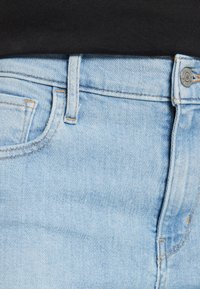 Jeans de mezclilla azul claro con un bolsillo frontal visible, presilla para cinturón, botón de metal y una parte superior oscura metida en la cintura.