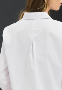 Witte blouse met een rugplooi, gladde textuur en een schoon ontwerp, met minimalistische kenmerken en een op maat gesneden pasvorm.