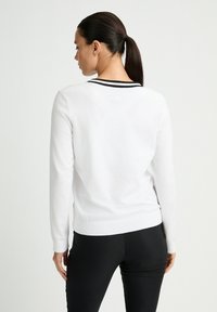 Weißer Pullover mit langen Ärmeln und einem schwarzen gestreiften Kragen. Das Material sieht weich aus und er hat eine taillierte Form.