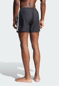Svarte svømmeshorts med elastisk midjebånd og tre hvite sidestreker, laget av lett stoff, med en avslappet passform.