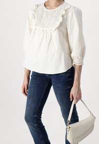 Blusa blanca y ligera con detalle de volantes bordados y mangas de 3/4. Combinada con unos pantalones de mezclilla oscuros y un bolso estructurado en color crema.