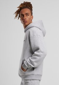 Pilkos spalvos džemperis, pagamintas iš minkšto medvilnės pluošto, turi kengūros kišenę, surištas rankoves ir apykaklę, taip pat logotipą ant krūtinės.