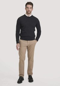 Dunkelgrauer Pullover, khakifarbene Hose, schwarze Slipper. Das Modell trägt einen körperbetonten, rundhalsigen Pullover und ein Hemd mit Kragen darunter.