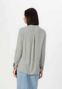 Camicia a maniche lunghe a righe verticali verdi e bianche, con orlo arrotondato e polsini con bottoni. Tessuto morbido e leggero.