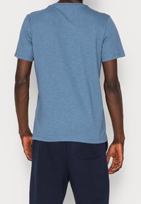 Modrý krátký rukáv T-shirt z jemného, strukturovaného materiálu s kulatým výstřihem. Má uvolněný střih a zakřivený lem.