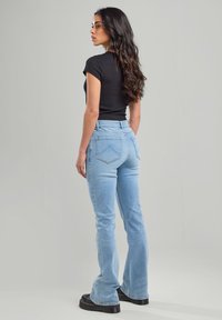 Helle blaue Marlenejeans mit hoher Taille, Vorder- und Hintertaschen sowie einer verwaschenen Optik, kombiniert mit einem figurbetonten schwarzen T-Shirt und Plateauschuhen.