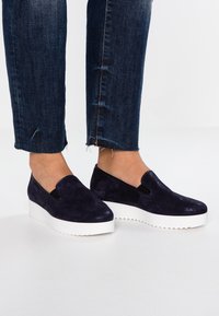 Navy modré semišové slip-on boty s elastickými bočními panely, s tlustou bílou platformovou podešví a zaobleným designem špičky.