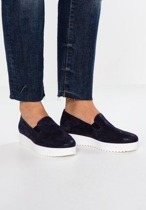 Laivastonsiniset mokka-slip-on-kengät, joissa on joustavat sivupaneelit, paksu valkoinen alustapaketti ja pyöreä kärki.