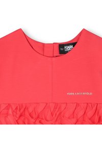 Κοραλί φόρεμα με στρογγυλή λαιμόκοψη, με υφαντό ύφασμα και βολάν τούλι στην άκρη. Η ετικέτα "KARL LAGERFELD" είναι ορατή.