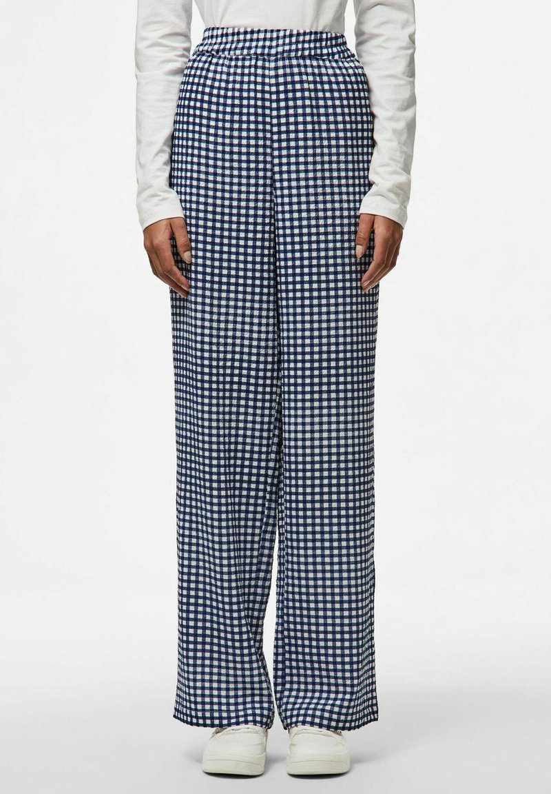 Navy och vit rutiga vida byxor med elastisk midja, gjorda i lätt tyg, tillsammans med vita sneakers.