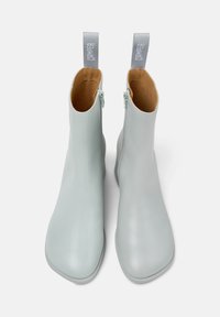 Botines de cuero azul claro con punteras cuadradas, cremalleras laterales y tiradores grises. Textura suave, diseño minimalista e interior en color marrón claro.