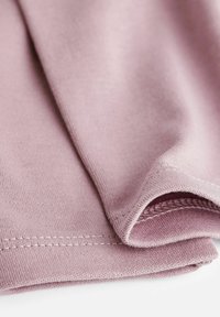 Minkštas, rožinis audinys su lygiu paviršiumi, turintis išlenktą apvadą ir tvirtą siuvimą kraštuose, šiek tiek lenkiasi per save.