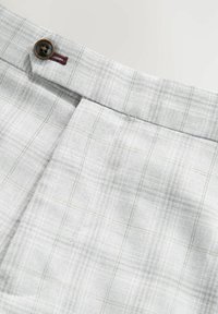Pantaloni a quadri grigi chiari con una finitura texture, caratterizzati da un bottone marrone e linee sottili gialle e bianche nel motivo.