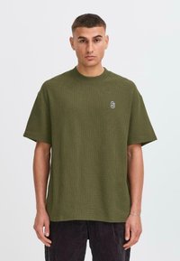 Olive green waffle-knit t-shirt with a round neckline and short sleeves, featuring a small logo detail on the chest.