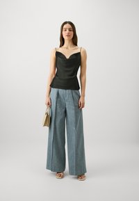 Camisola nera in satin con scollatura a cuore, abbinata a pantaloni in denim chiaro a gamba larga. Porta una borsa color cuoio e indossa sandali beige.