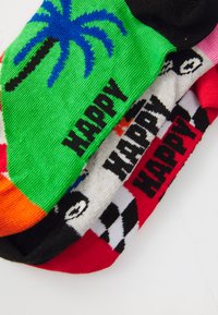 Színes zoknik különböző mintákkal: zöld pálmafás, piros, fekete-fehér kockás, a "HAPPY" szó vastag betűkkel.