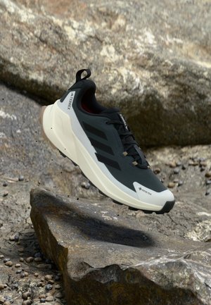 Scarpe da esterno nere e grigie con tomaia testurizzata, caratterizzate da tre strisce nere, una suola intermedia bianca e marchio Gore-Tex.