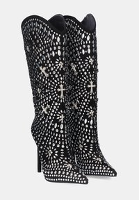 Botas negras de tacón alto con puntera puntiaguda, que presentan un diseño con tachuelas y acentos metálicos, adornadas con patrones en forma de cruz a lo largo.