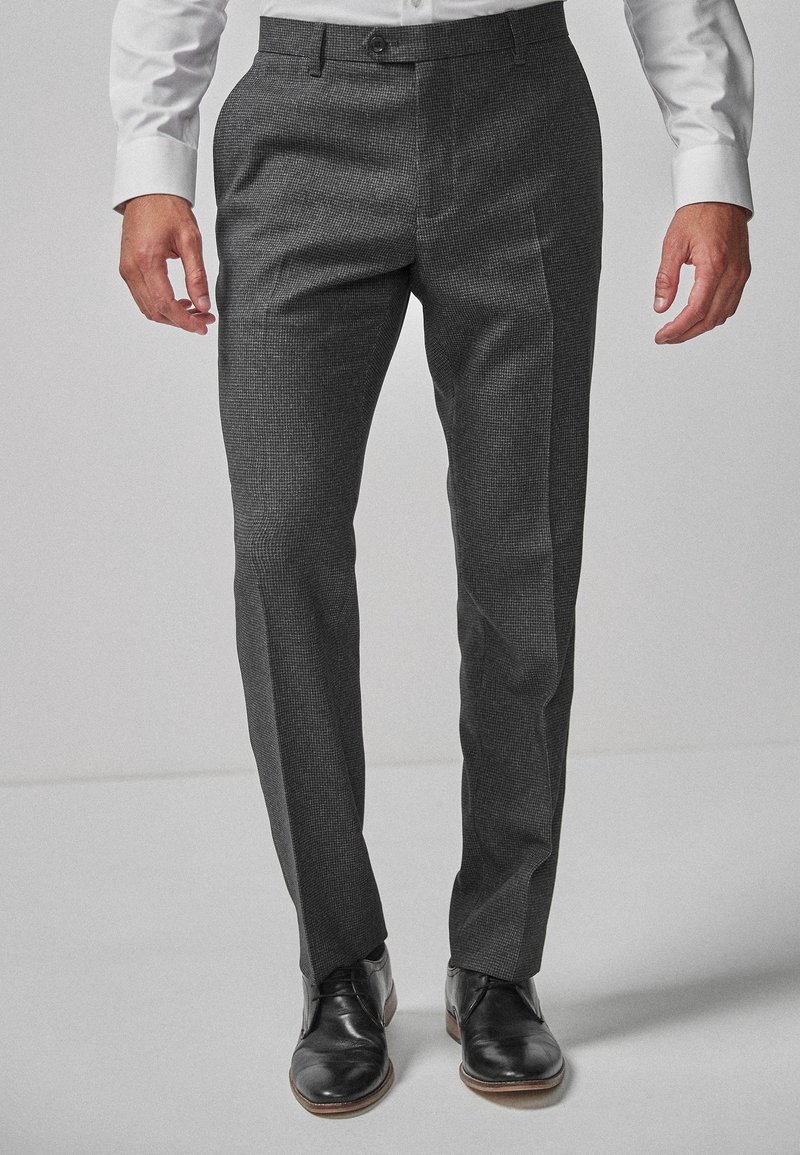 Homme portant un pantalon habillé slim-fit à carreaux gris foncé, associé à des chaussures en cuir noires et une chemise blanche.