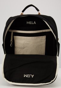 Mochila de tela preta com um interior creme, apresentando um bolso com fecho, um compartimento grande e etiquetas impressas "MELA" e "A7AM."