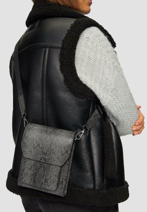 Szara torebka typu crossbody ze skóry węża z klapką, regulowanym paskiem i srebrnymi elementami, noszona na czarnym skórzanym kamizelce z futrzanym wykończeniem.