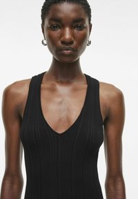 Sort, ribbet tanktop uden ærmer med en dyb V-udskæring og en tætsiddende pasform. Glat tekstur med minimal hardware eller detaljer.