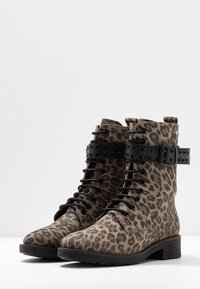 Botas de tobillo con estampado de leopardo, hechas de ante, con cordones negros, una correa negra con tachuelas alrededor del tobillo y un tacón bajo.