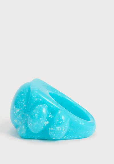 Δαχτυλίδι από μπλε ρητίνη με λευκές κηλίδες, που διαθέτει τρία στρογγυλεμένα ανασηκωμένα σχήματα στην κορυφή, σε απλό λευκό φόντο.