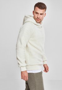 Off-white fleecegenser med teksturert finish, kengurulomme og ribbede mansjetter. Ledig passform med fastsydd hette.