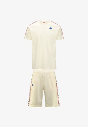 Completo sportivo color crema composto da una T-shirt a maniche corte e pantaloni shorts. Presenta un logo blu e strisce laterali rosse su entrambi i pezzi. Tessuto leggero.