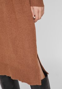 Abito marrone a maglia con polsini e orlo a costine. Le spacchi laterali migliorano la libertà di movimento, mentre la texture liscia offre un aspetto casual ma strutturato.